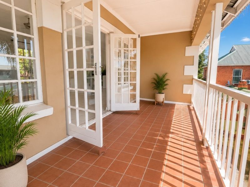 A well-maintained covered balcony featuring terracotta tiling, white balustrades, and classic French doors providing seamless access to the interior living space.