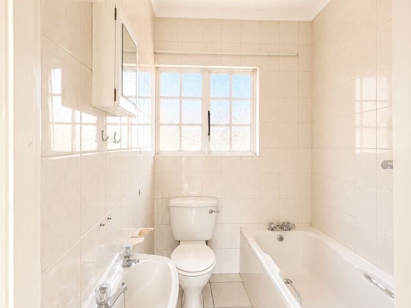 A clean, functional bathroom featuring a wall-mounted basin, toilet, and bathtub with full-height wall tiling and neutral floor tiles.