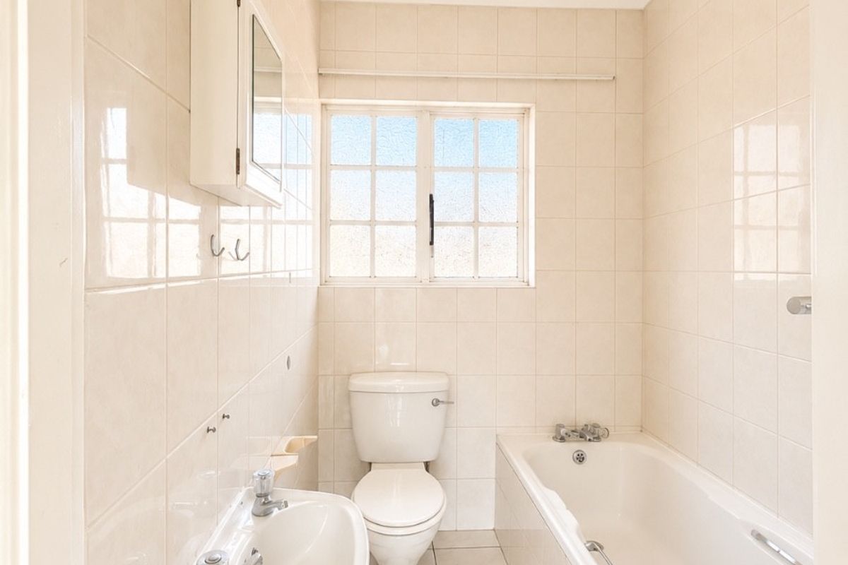 A clean, functional bathroom featuring a wall-mounted basin, toilet, and bathtub with full-height wall tiling and neutral floor tiles.
