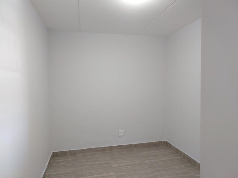 A clean, empty bedroom featuring neutral white walls and modern wood-look tiled flooring, providing a versatile blank canvas for any interior design style.