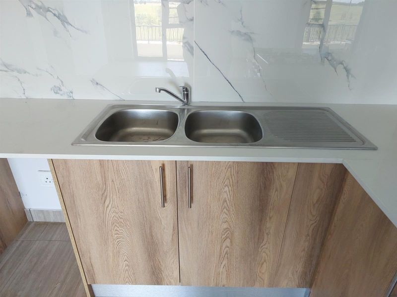 A modern kitchen area featuring a double bowl stainless steel sink, stone countertops, and marble-look splashback tiles with wood-finish cabinetry.