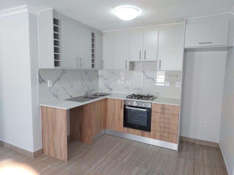 Modern kitchen featuring light wood-tone lower cabinets, white upper cabinetry, marble-look splashback, gas hob, and built-in oven in a clean, well-maintained space.