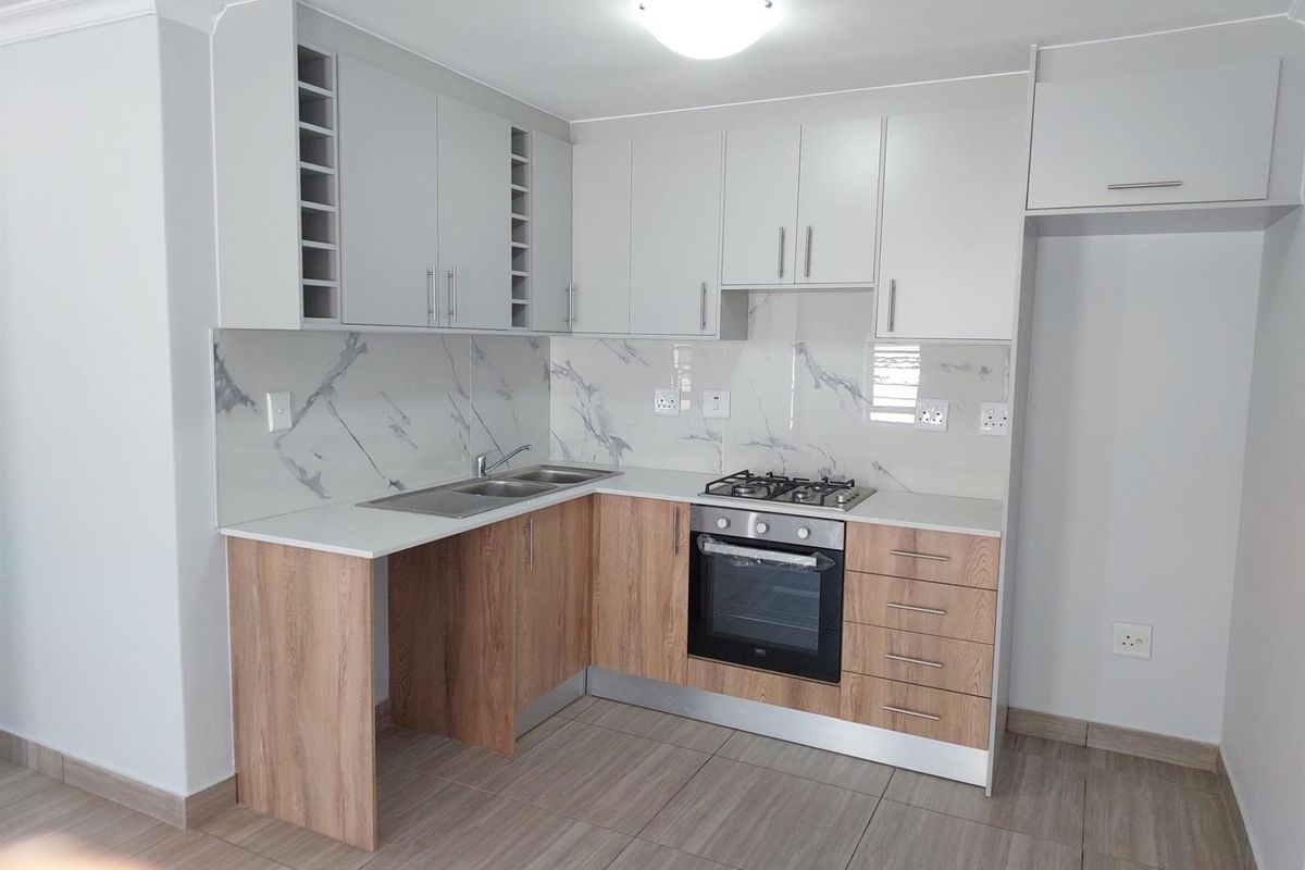 Modern kitchen featuring light wood-tone lower cabinets, white upper cabinetry, marble-look splashback, gas hob, and built-in oven in a clean, well-maintained space.