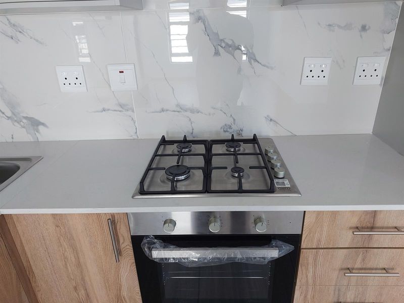 Modern kitchen featuring a clean quartz countertop, marble-look splashback, and integrated stainless steel gas hob and oven with wood-finish cabinetry.