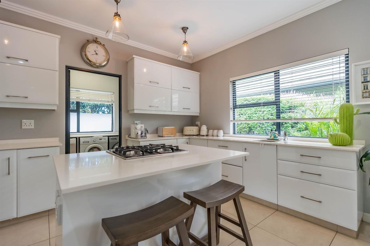 Modern kitchen featuring white cabinetry, stone countertops, a central island with a built-in gas hob, and large windows overlooking the garden.