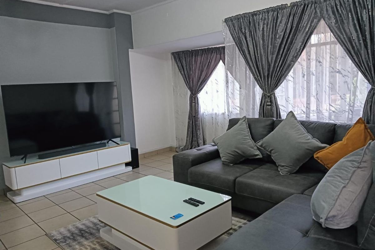 A comfortable living room featuring tiled flooring and large windows with decorative curtains, providing a bright and functional space for relaxation.