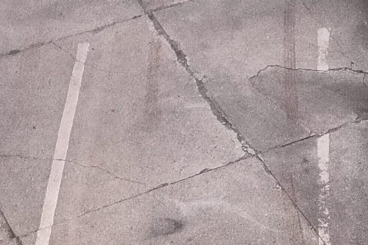 An elevated view of a weathered concrete parking area showing significant surface cracking and worn bay markings.
