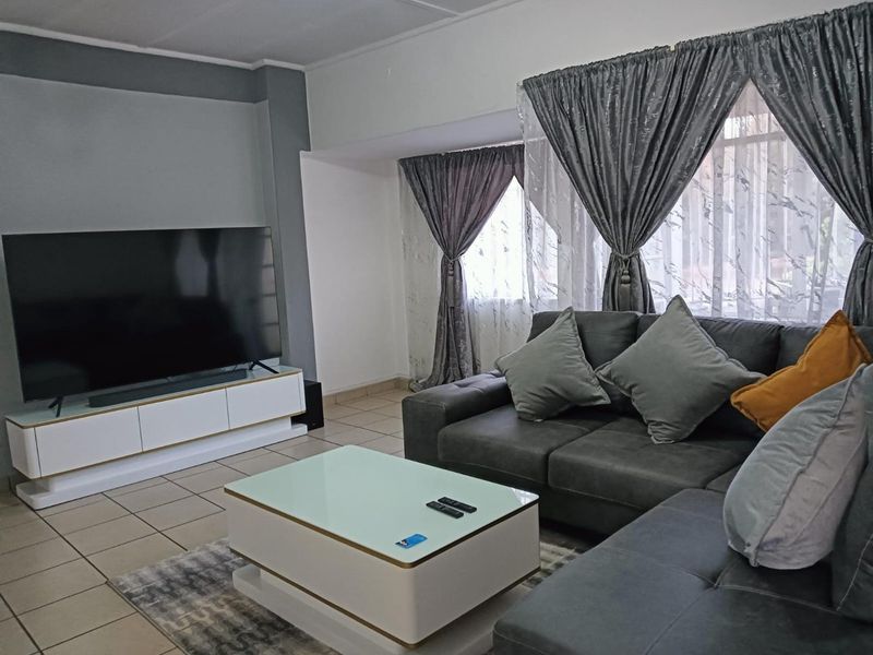 A comfortable living room featuring tiled flooring and large windows with decorative curtains, providing a bright and functional space for relaxation.