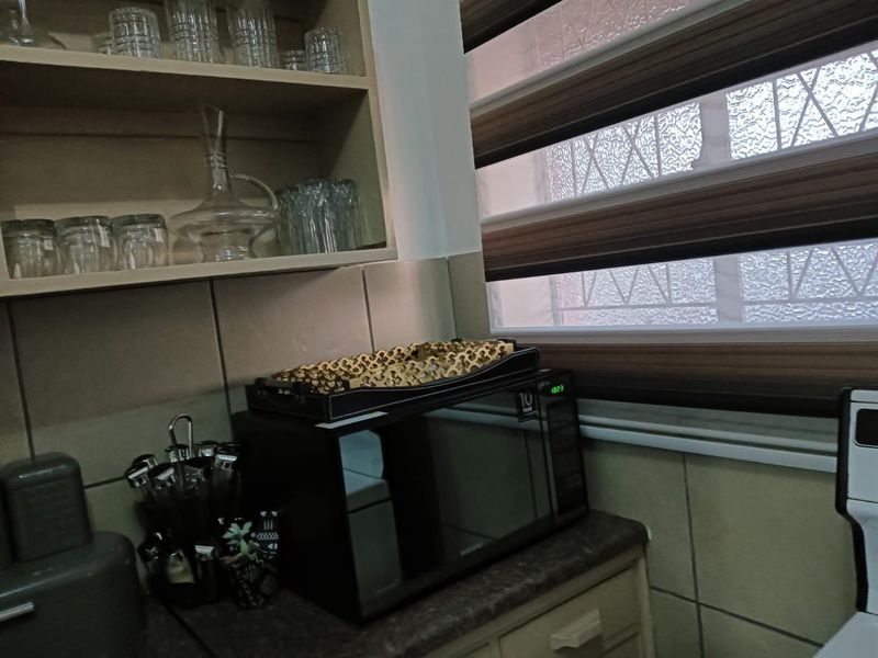 A functional kitchen corner featuring built-in cabinetry, tiled splashbacks, and a window with modern zebra blinds.