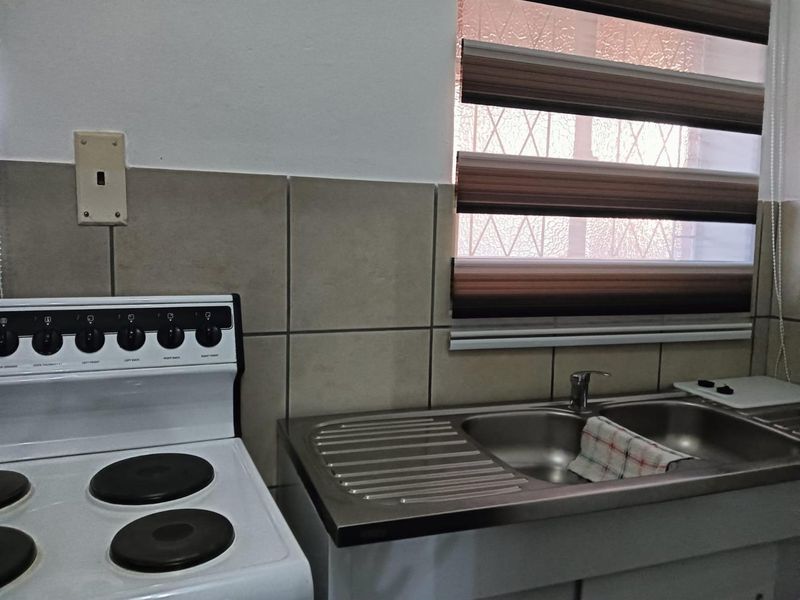 Compact kitchen area featuring a stainless steel sink, tiled backsplash, and a freestanding electric stove.