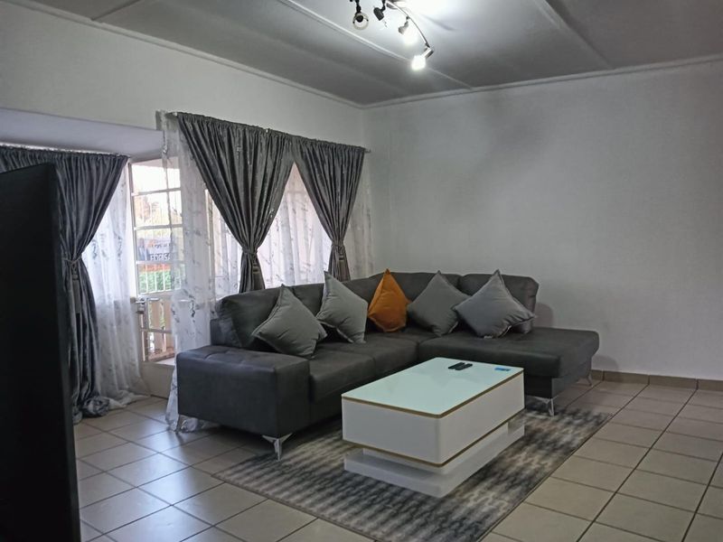 A living room featuring tiled flooring and a glass door leading to an outdoor area, providing natural light to the space.