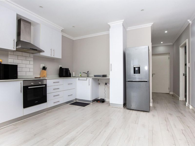 Modern kitchen featuring white cabinetry, subway tile backsplash, built-in oven, stainless steel extractor fan, and light-toned laminate flooring in an open-plan layout.