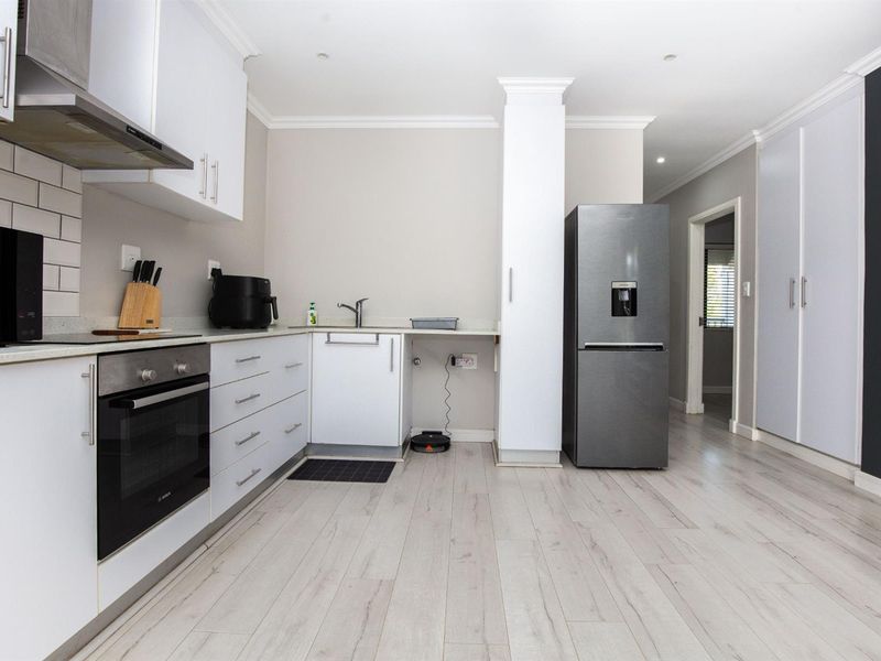 Modern kitchen featuring white cabinetry, subway tile backsplash, built-in oven and hob, and light-toned laminate flooring in an open-plan layout.