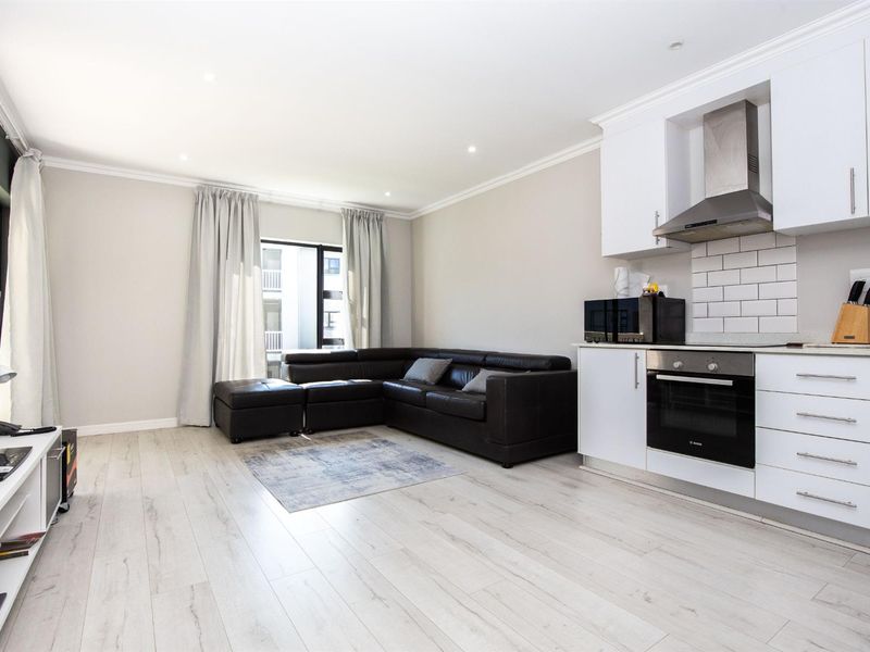 Modern open-plan living area featuring a sleek kitchen with built-in oven, extractor fan, and subway tile backsplash, complemented by light laminate flooring throughout.