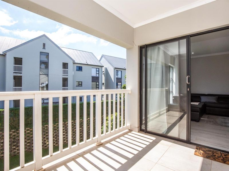 A clean, covered balcony featuring tiled flooring and a white balustrade railing, providing a seamless transition to the interior living space via sliding glass doors.