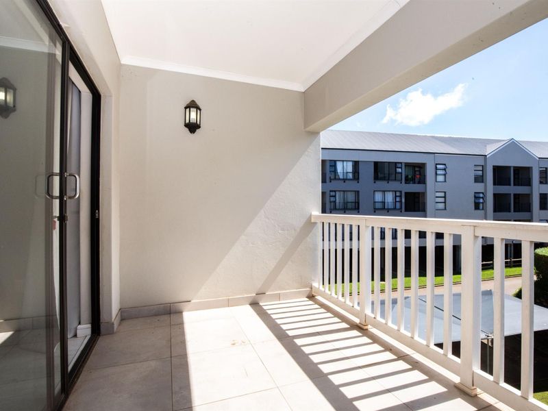 A clean, covered balcony featuring tiled flooring, a white railing, and a sliding glass door providing access to the apartment interior.