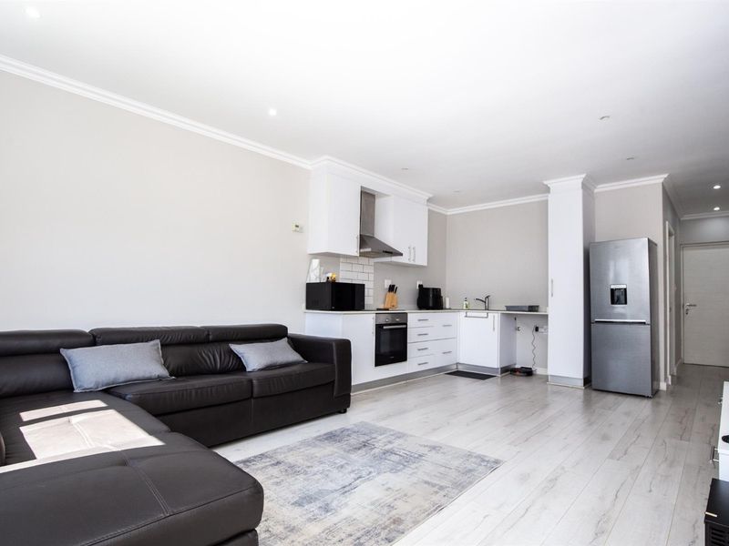 Modern open-plan living area featuring a sleek kitchen with built-in appliances, subway tile backsplash, and light laminate flooring throughout.