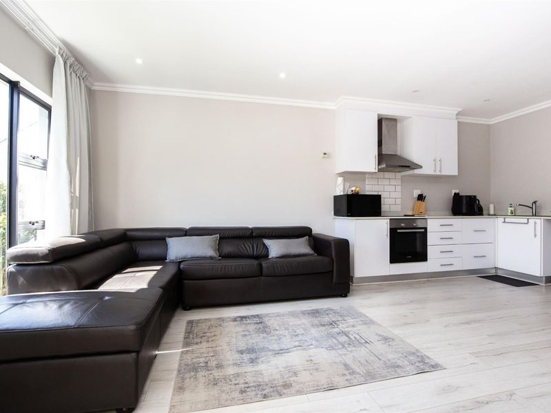Modern open-plan living area featuring a sleek kitchen with built-in appliances, subway tile backsplash, and light laminate flooring, leading to a bright outdoor space.