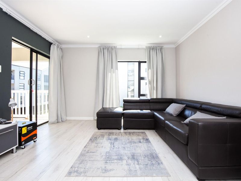 A bright and modern living room featuring light laminate flooring, crown molding, and large sliding glass doors leading to an outdoor balcony area.