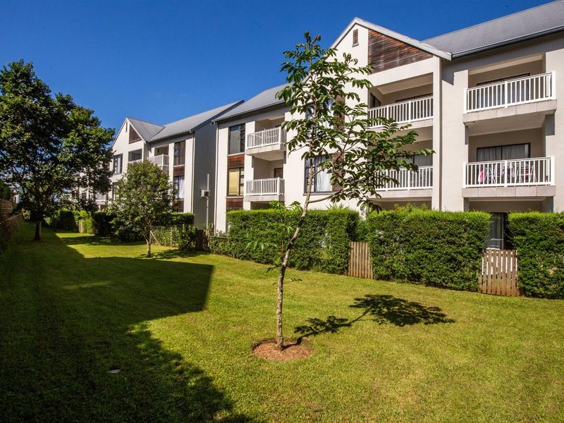 Rear view of the apartment complex featuring well-maintained communal gardens, landscaped hedging, and private balconies with metal railings.