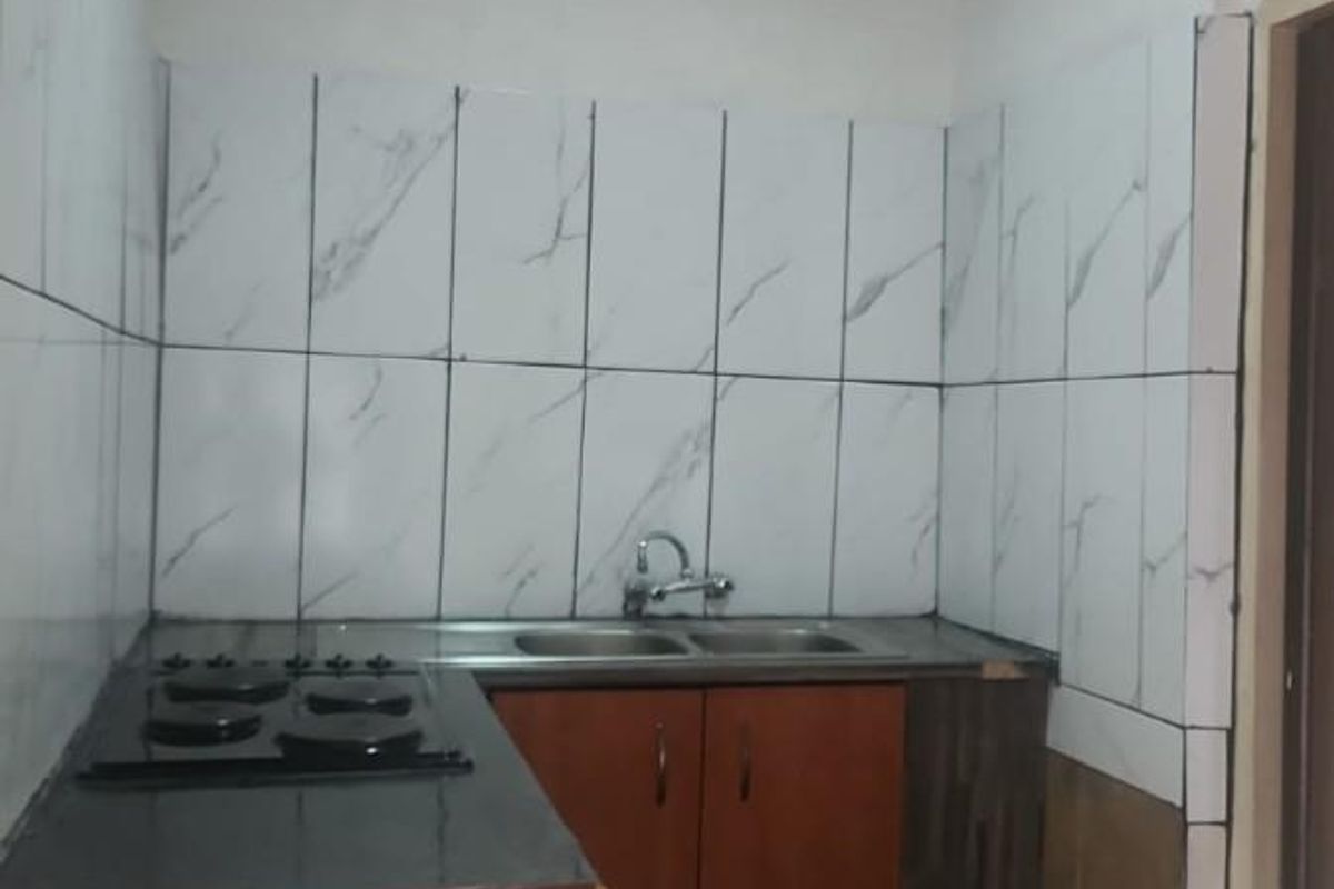 A compact kitchen featuring built-in cabinetry, a gas hob, and a stainless steel sink with marble-effect wall tiling.