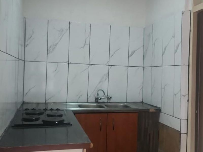 A compact kitchen featuring built-in cabinetry, a gas hob, and a stainless steel sink with marble-effect wall tiling.