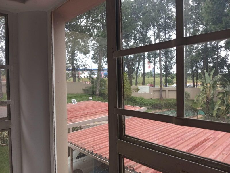 A view from an interior window looking out over a complex with corrugated metal roofing and surrounding trees.