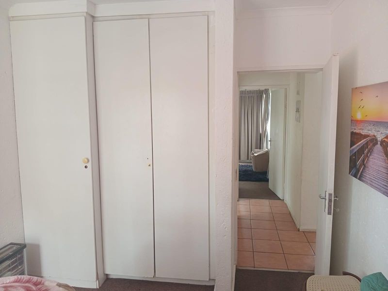 A bedroom featuring built-in cupboards with a view through the doorway into an adjacent tiled hallway and living area.