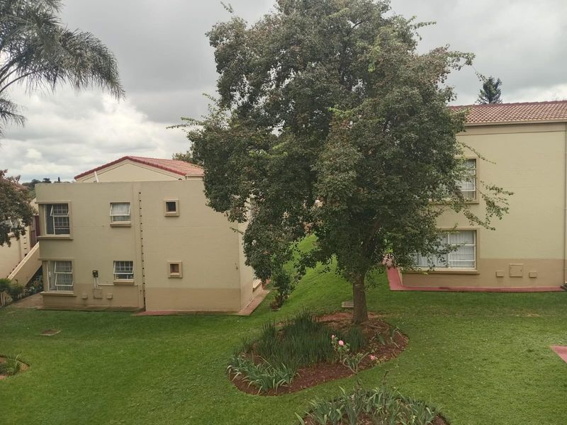 A view of the apartment complex exterior featuring well-maintained garden areas, mature trees, and classic plastered building facades with tiled roofing.