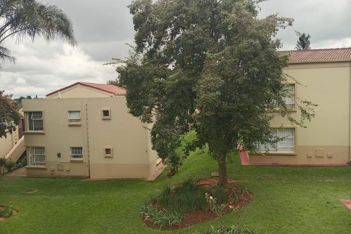 A view of the apartment complex exterior featuring well-maintained garden areas, mature trees, and classic plastered building facades with tiled roofing.