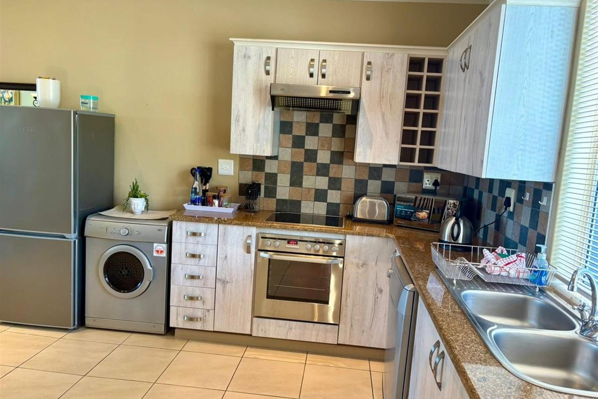 Functional kitchen featuring light wood-grain cabinetry, granite countertops, built-in oven, hob, extractor fan, and double stainless steel sink with tiled flooring.