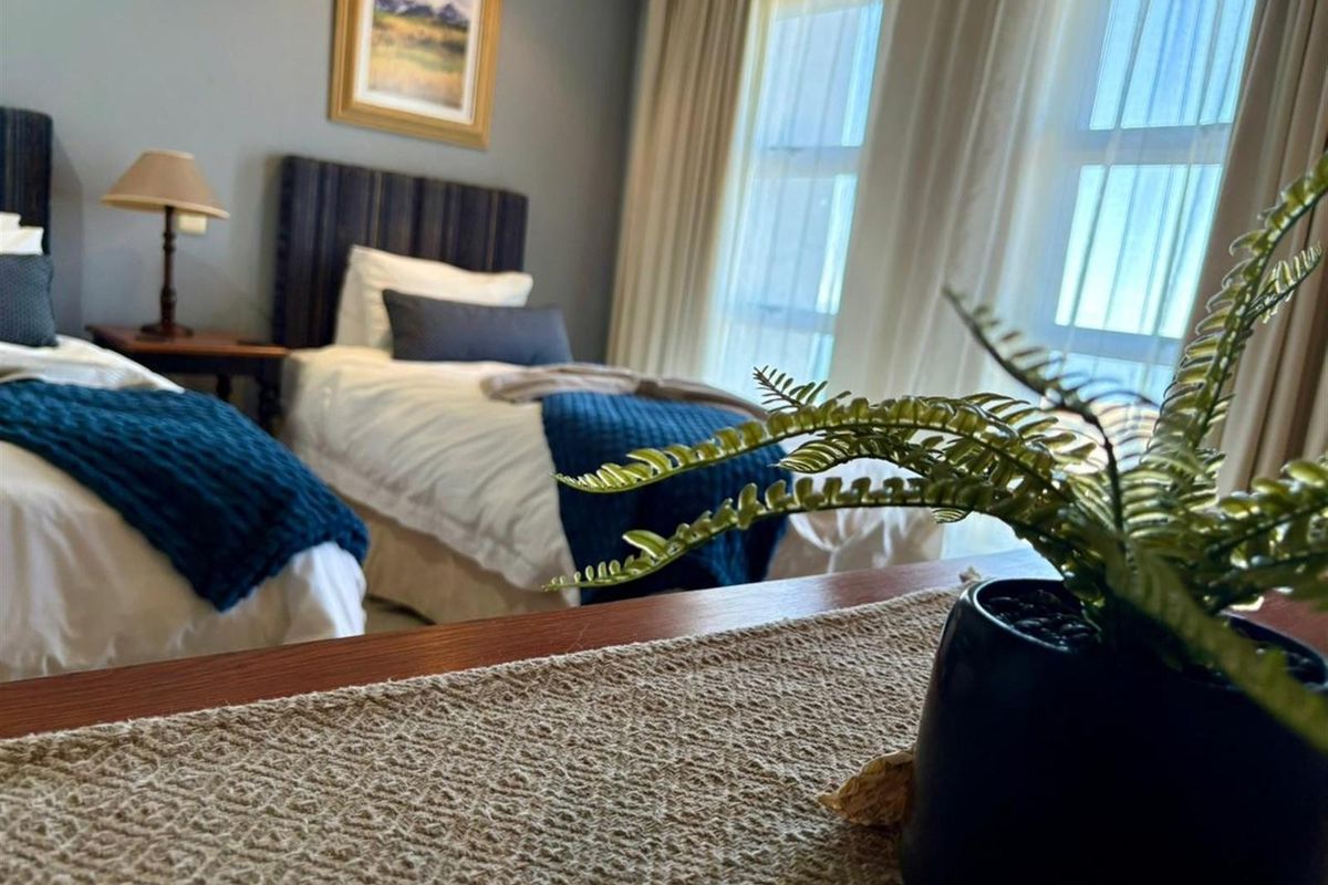 A bedroom featuring large windows with natural light, neutral wall tones, and space for twin beds.