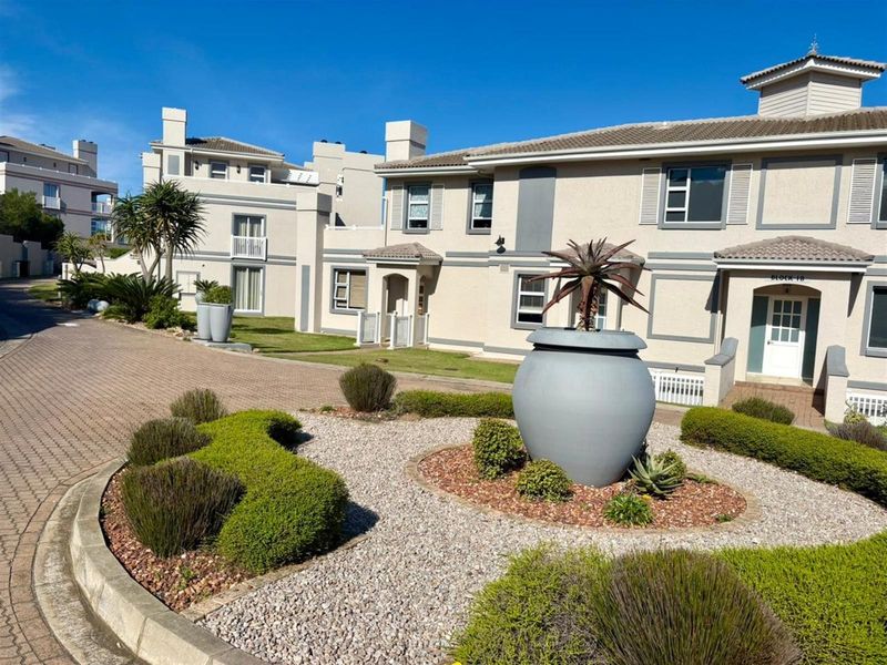 Exterior view of a townhouse complex featuring paved driveways, landscaped garden beds, and well-maintained building facades with tiled roofing.