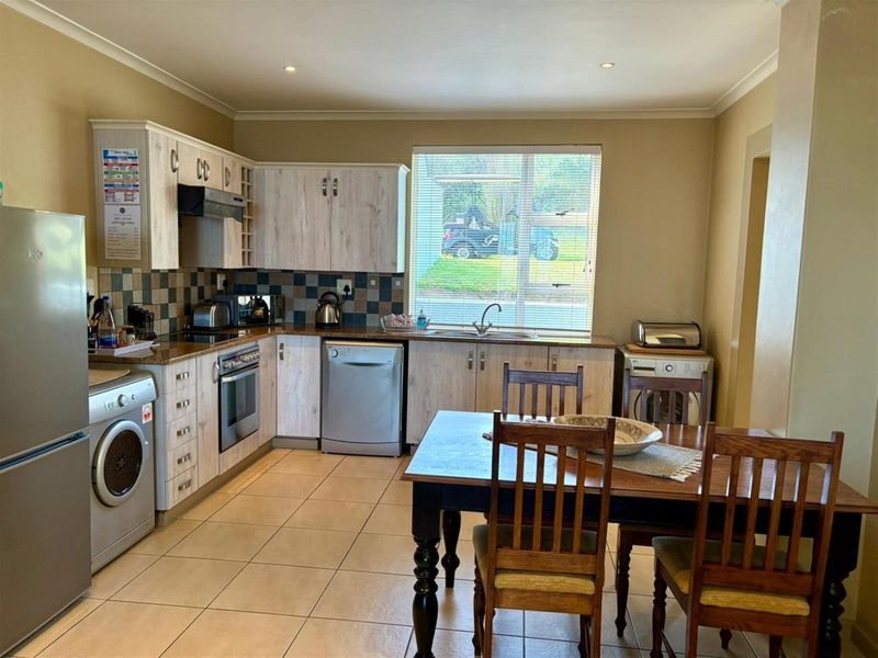 Open-plan kitchen featuring light wood-grain cabinetry, tiled flooring, built-in oven, extractor fan, and a double sink, seamlessly flowing into the dining area.