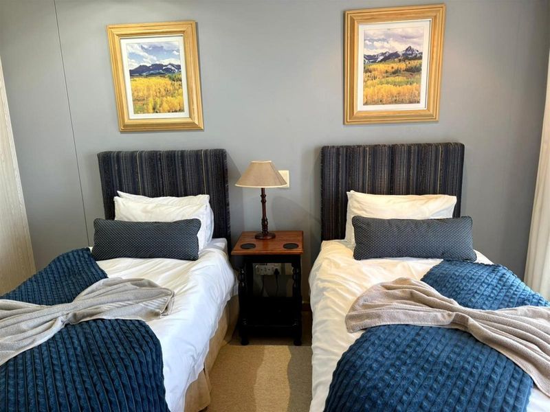 A well-maintained bedroom featuring neutral wall tones, carpeted flooring, and space for twin beds with a central bedside table.