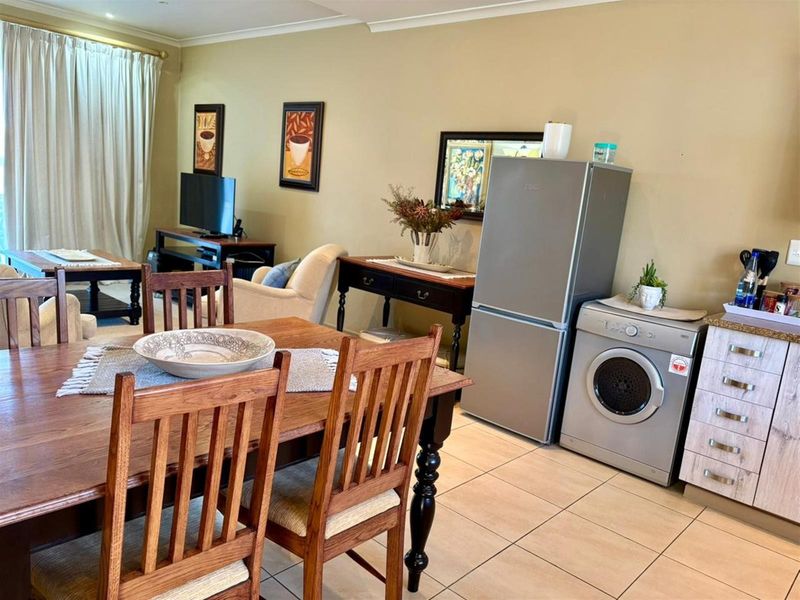 Open-plan living and dining area featuring tiled flooring, neutral wall tones, and integrated kitchen cabinetry with space for laundry appliances.