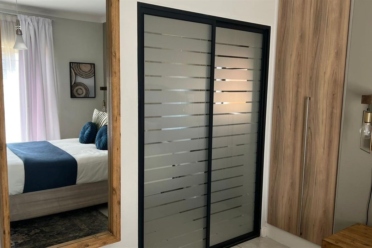 A well-maintained bedroom featuring modern built-in wardrobes with wood-look finishes and a contemporary frosted glass sliding door.