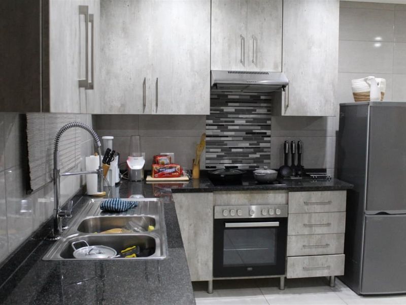 Modern kitchen featuring granite countertops, built-in oven, electric hob, extractor fan, and contemporary cabinetry with a tiled backsplash.