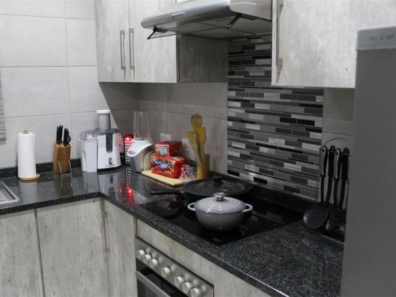 A modern kitchen featuring granite countertops, fitted cabinetry, a built-in oven with electric hob, and a stylish tiled backsplash.