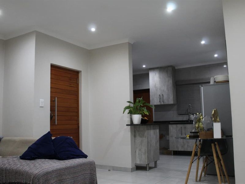 Open-plan living area featuring modern grey cabinetry, stone countertops, recessed downlighting, and tiled flooring, seamlessly connecting to the main entrance.
