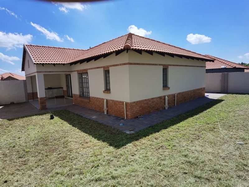 Rear view of the house featuring a terracotta tiled roof, brick-accented exterior walls, a covered patio area, and a surrounding garden with paved pathways.