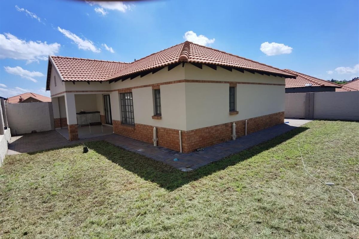 Rear view of the house featuring a terracotta tiled roof, brick-accented exterior walls, a covered patio area, and a surrounding garden with paved pathways.