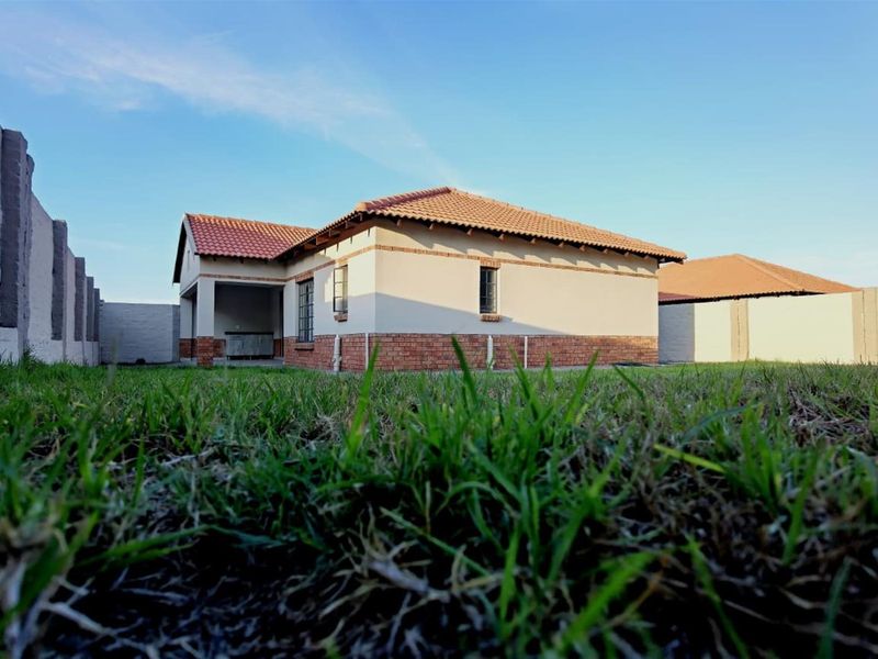 A view of the rear elevation of the house featuring a brick and plaster facade, tiled roof, and a covered patio area overlooking the lawn.
