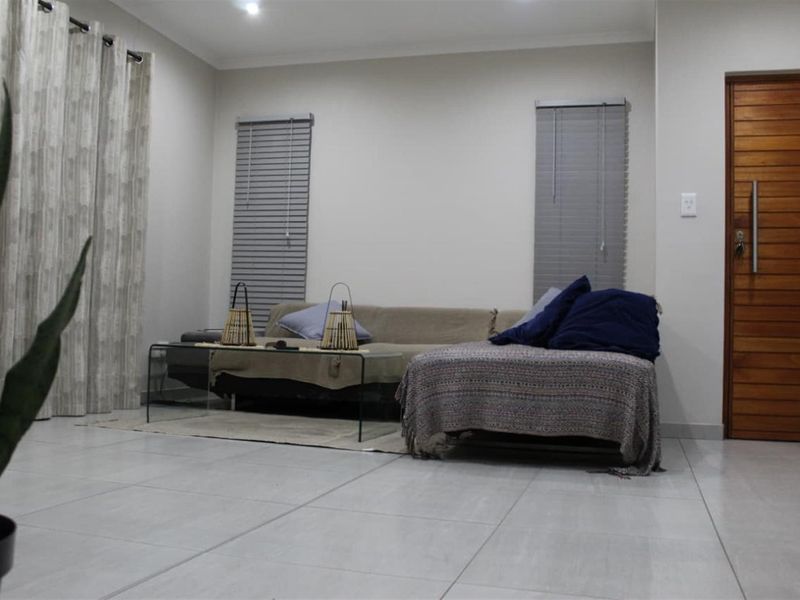 A well-lit living room featuring neutral tiled flooring, modern recessed downlights, and a solid timber entrance door with venetian blinds.