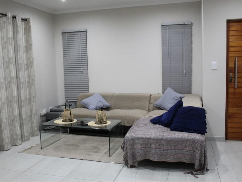 A well-maintained living room featuring neutral tiled flooring, modern venetian blinds, and a solid timber entrance door.