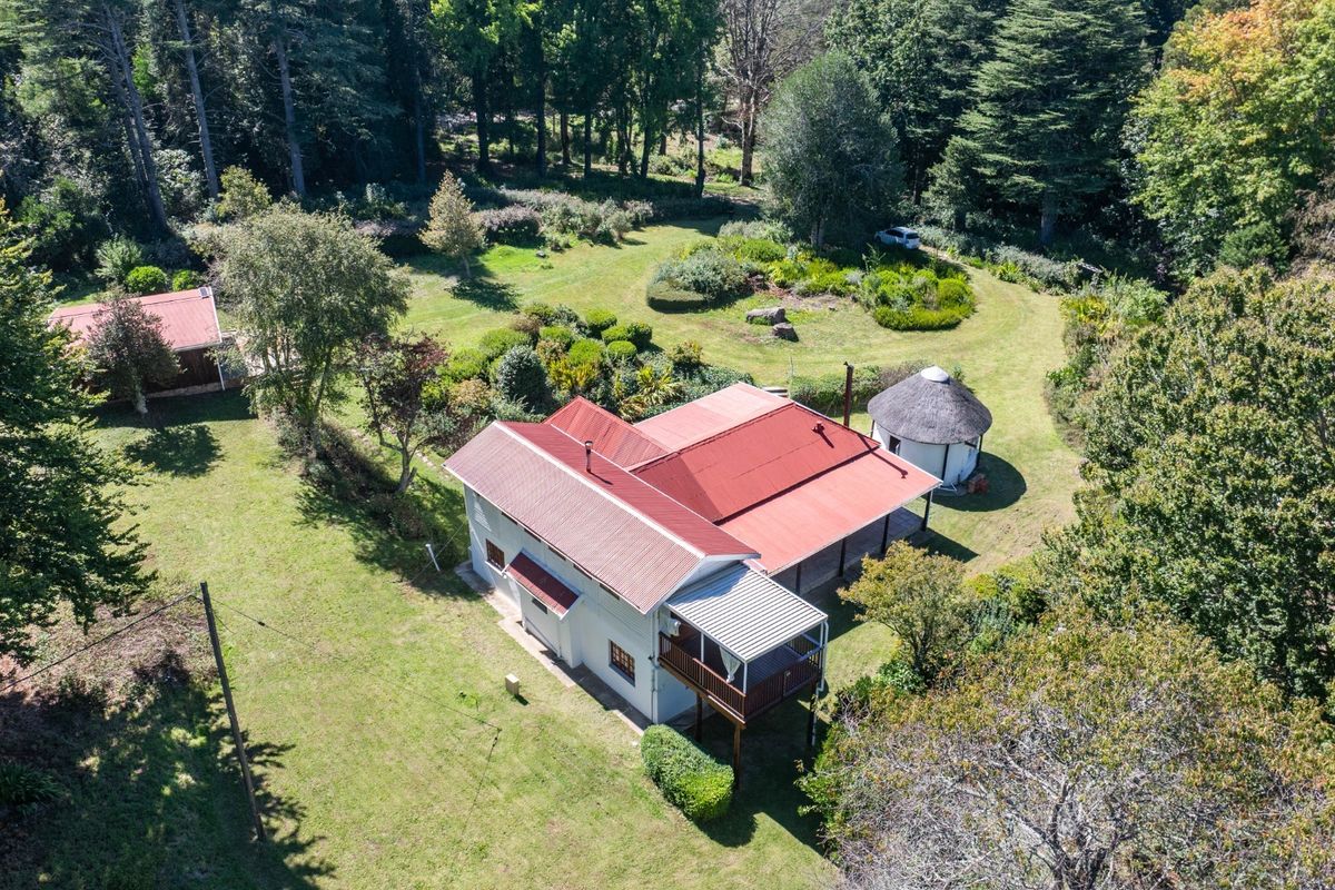 Aerial view of a residential property featuring a main house with a metal roof, a separate thatched outbuilding, and extensive landscaped garden grounds.