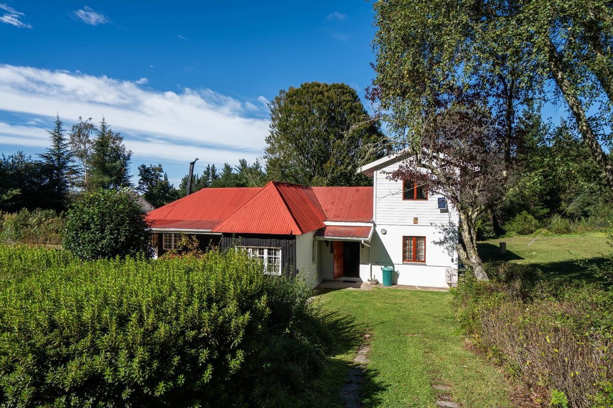 Rear view of a two-story house featuring a red corrugated metal roof, white timber siding, and a surrounding garden area.