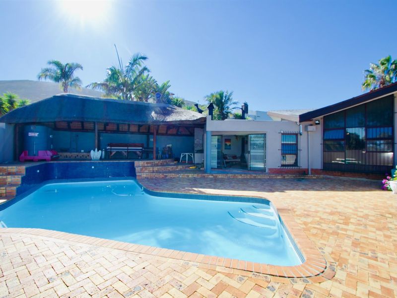 Outdoor pool area featuring a swimming pool with tiled surround, brick paved patio, and a covered thatched entertainment area.