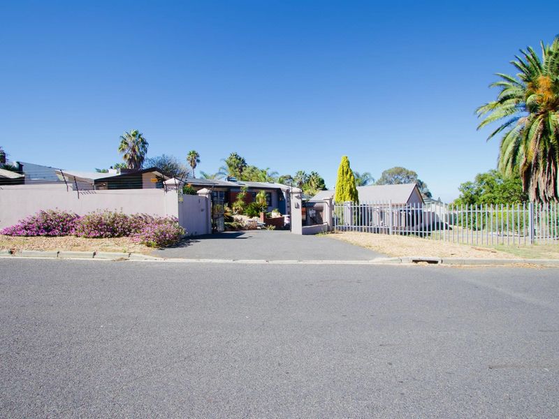Street view of the property entrance featuring a paved driveway, perimeter boundary walls, and metal security fencing.