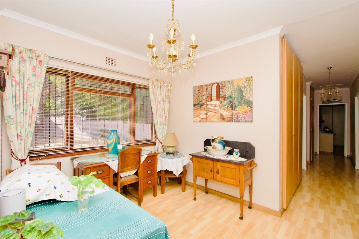 A well-maintained bedroom featuring light wood-look flooring, built-in cupboards, and a large window with venetian blinds, leading into a hallway.